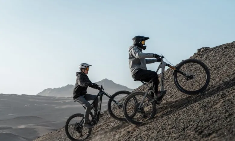 Two cyclists ride AmFlow e-bikes uphill on a rocky, desert terrain.