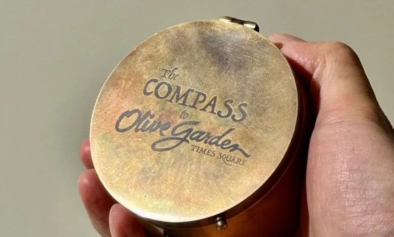 Hand holding a compass pointing to Olive Garden Times Square.