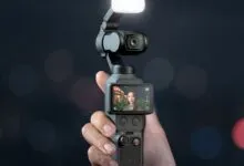 Hand holding DJI Osmo Pocket 3 camera with screen showing a woman.