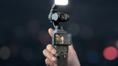 Hand holding DJI Osmo Pocket 3 camera with screen showing a woman.