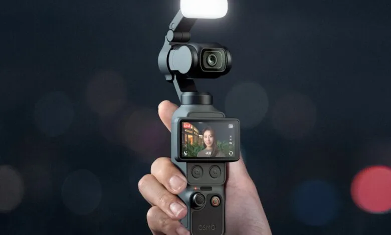 Hand holding DJI Osmo Pocket 3 camera with screen showing a woman.