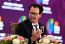 Dario Amodei speaks at AI Impact Summit, wearing glasses and a suit.