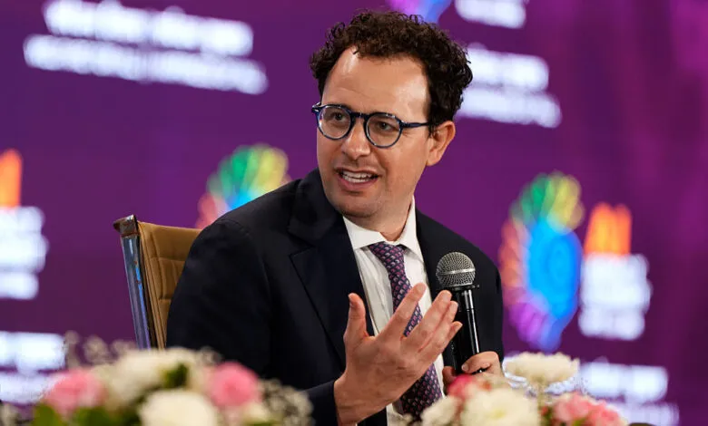 Dario Amodei speaks at AI Impact Summit, wearing glasses and a suit.