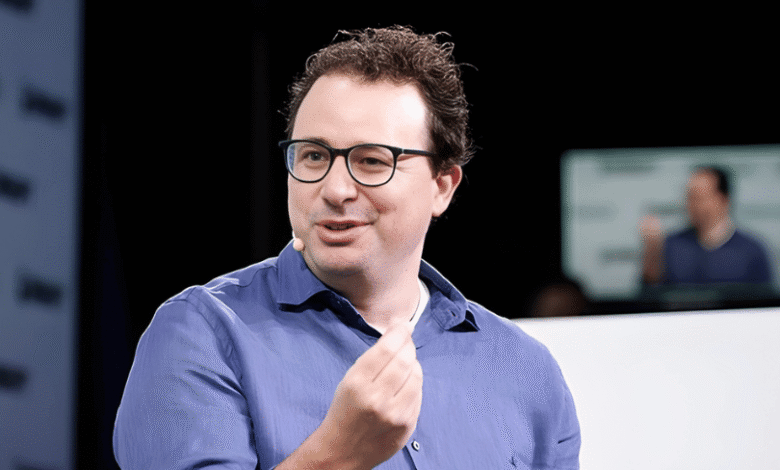 Dario Amodei speaks at a conference, wearing glasses and a blue shirt.