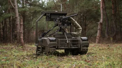 Military robot with mounted gun in forest setting.