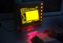 Retro computer with yellow screen and projected red laser keyboard.