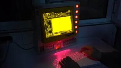Retro computer with yellow screen and projected red laser keyboard.