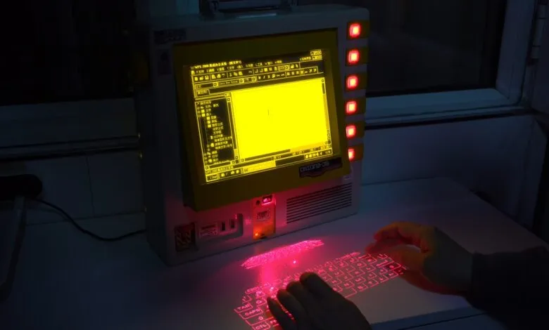 Retro computer with yellow screen and projected red laser keyboard.