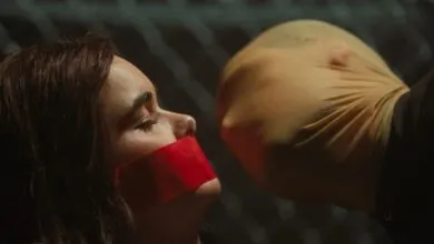 Woman with red tape over mouth faces person in stocking mask.