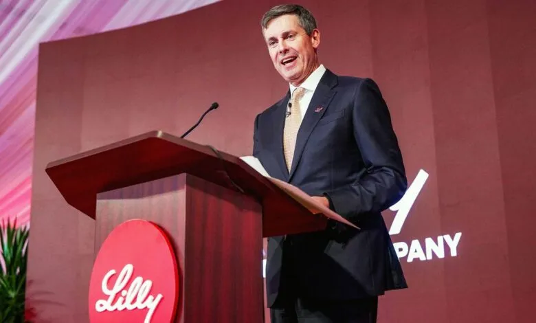 Man in suit speaks at podium with Lilly logo.