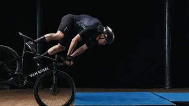 Cyclist in mid-air crash test on VAN RYSEL bike, preparing to land on mats.