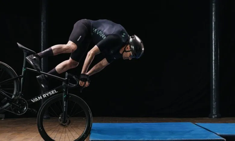 Cyclist in mid-air crash test on VAN RYSEL bike, preparing to land on mats.
