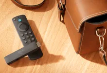 Amazon Fire TV Stick and remote on a wooden surface with a brown leather bag.
