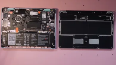 Two laptops, one disassembled showing internal components, on a pink surface.
