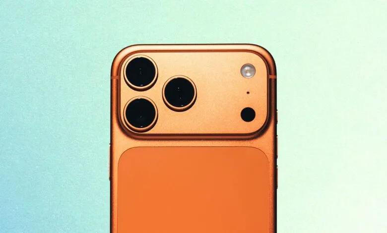 Close-up of an orange iPhone with three camera lenses on a light blue background.