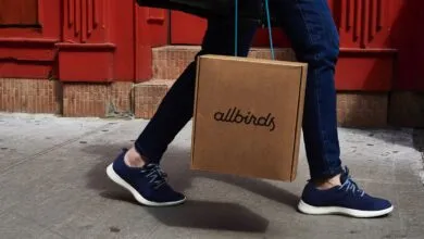 Person walking with Allbirds shoes and carrying an Allbirds box.