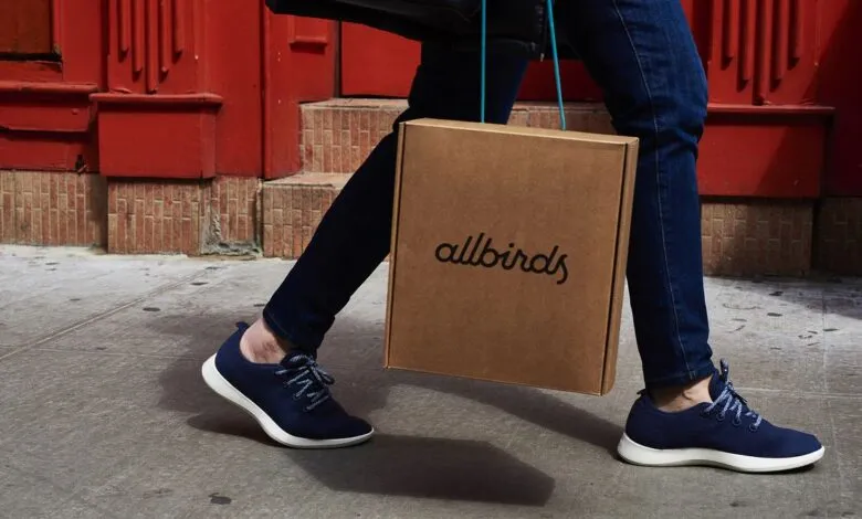 Person walking with Allbirds shoes and carrying an Allbirds box.