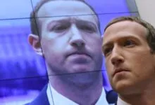 Mark Zuckerberg stands in front of a screen displaying his image.