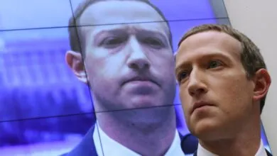 Mark Zuckerberg stands in front of a screen displaying his image.