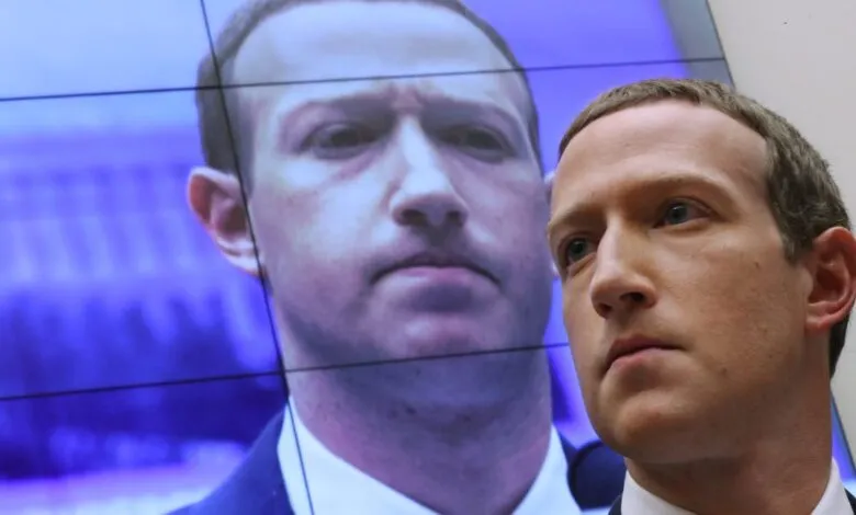 Mark Zuckerberg stands in front of a screen displaying his image.