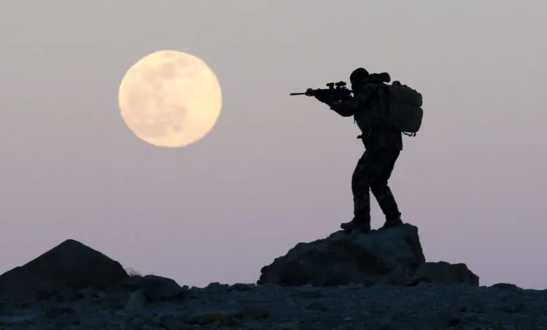 Silhouette of soldier aiming rifle against a full moon.