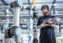 Technician controls robot arm in battery research, using tablet interface.