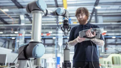 Technician controls robot arm in battery research, using tablet interface.