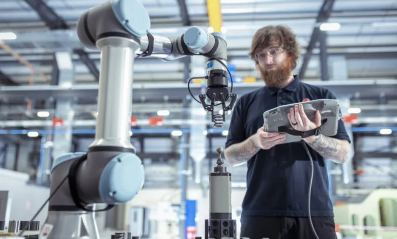 Technician controls robot arm in battery research, using tablet interface.