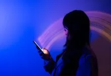 Woman illuminated by phone screen in blue and purple light.
