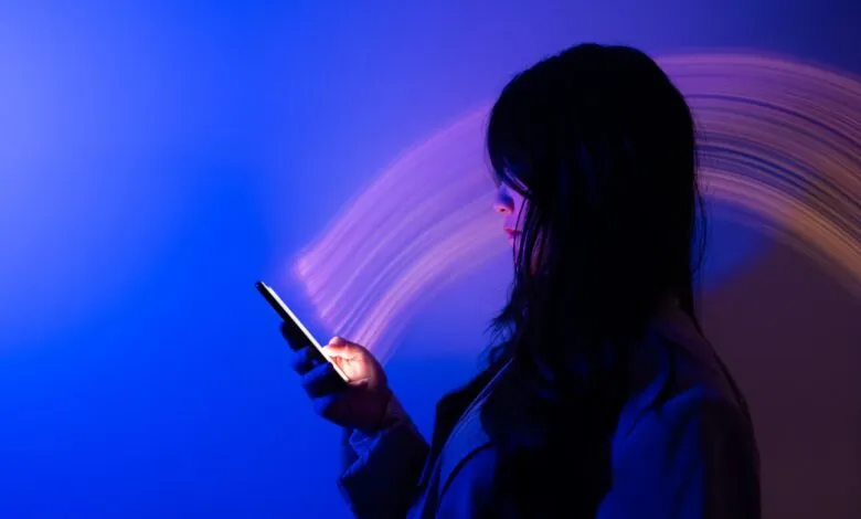 Woman illuminated by phone screen in blue and purple light.