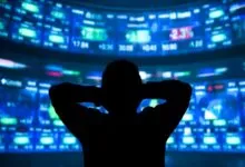 Silhouette of person watching stock market data on multiple screens.