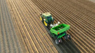 Aerial view of green tractor pulling planter across plowed field.