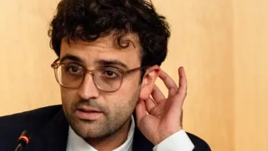 Man with glasses adjusts ear during a meeting.