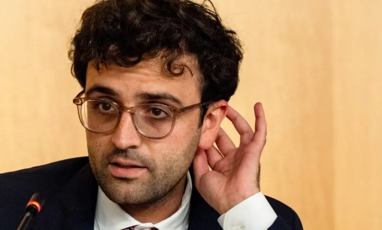 Man with glasses adjusts ear during a meeting.