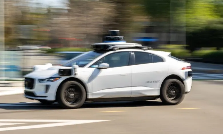 White Waymo self-driving car moving on a city street.