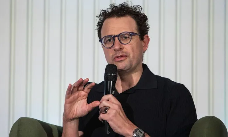 Nathan Fielder speaking into a microphone with hand gestures.