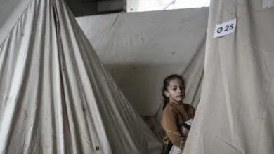 Young girl stands in tent with 'G 25' label, looking at camera.