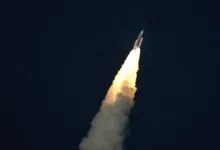 Rocket ascends against dark sky, propelled by bright exhaust plume.