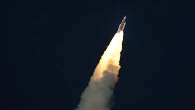 Rocket ascends against dark sky, propelled by bright exhaust plume.