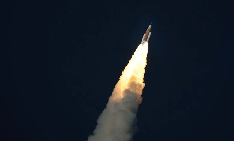 Rocket ascends against dark sky, propelled by bright exhaust plume.