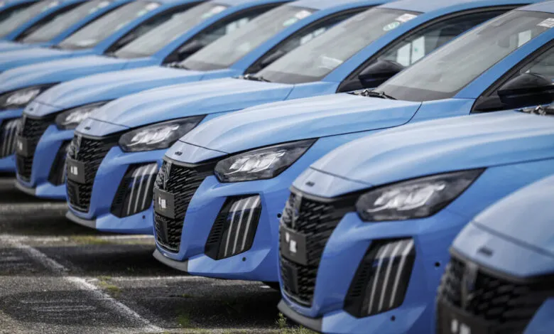 Row of identical blue Peugeot cars parked closely together.