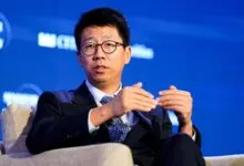 Man in suit with glasses gestures while speaking at a conference.