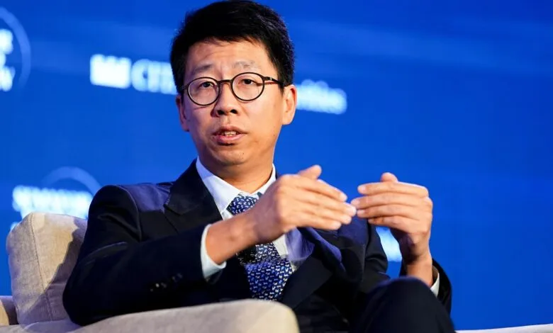 Man in suit with glasses gestures while speaking at a conference.