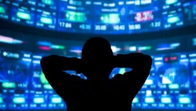 Silhouette of person watching stock market data on multiple screens.