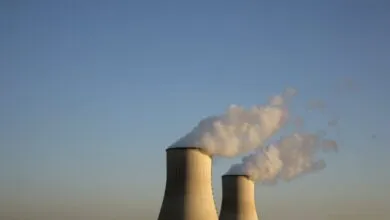 Two cooling towers emitting steam against a clear blue sky.