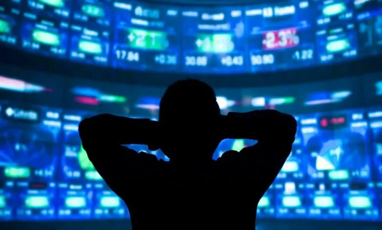 Silhouette of person watching stock market data on multiple screens.