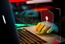 Hands type on laptop with digital shield, representing cybersecurity.