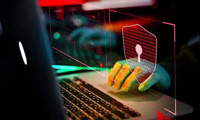 Hands type on laptop with digital shield, representing cybersecurity.