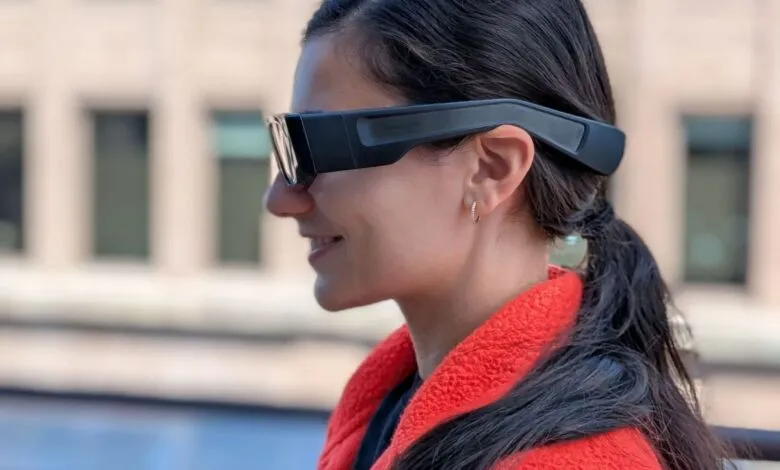 Woman wearing black augmented reality glasses with a red jacket outdoors.