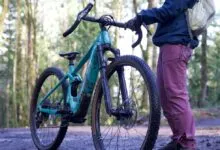 Person with teal mountain bike on a dirt trail in a forest setting.